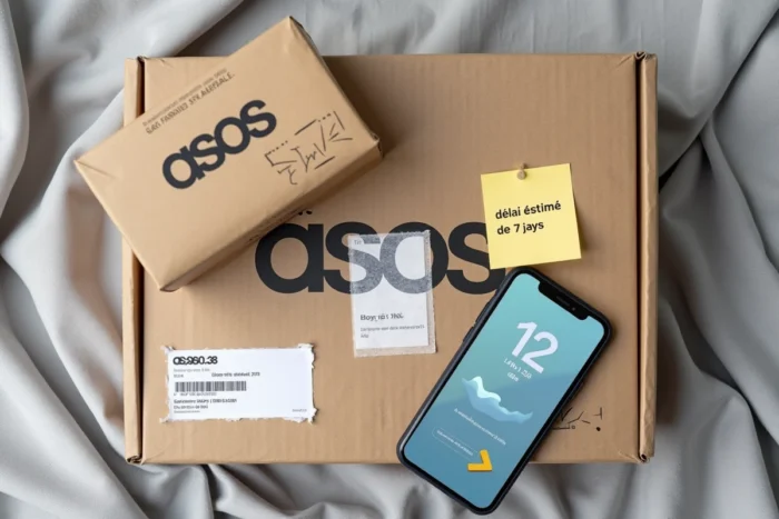 Flat lay d'un colis de mode en ligne avec un smartphone affichant un suivi de livraison et une note manuscrite sur les délais estimés